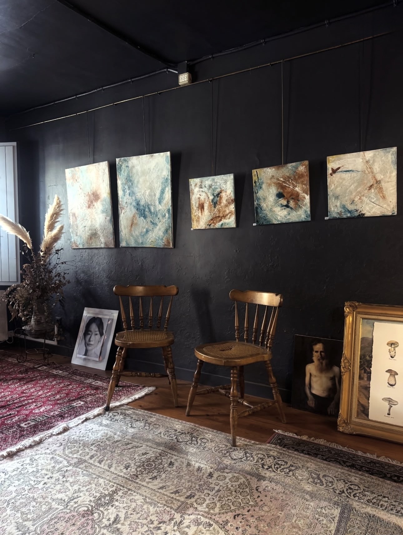 Sala de pared negra con una serie de pinturas abstractas colgadas sobre dos sillas de madera
