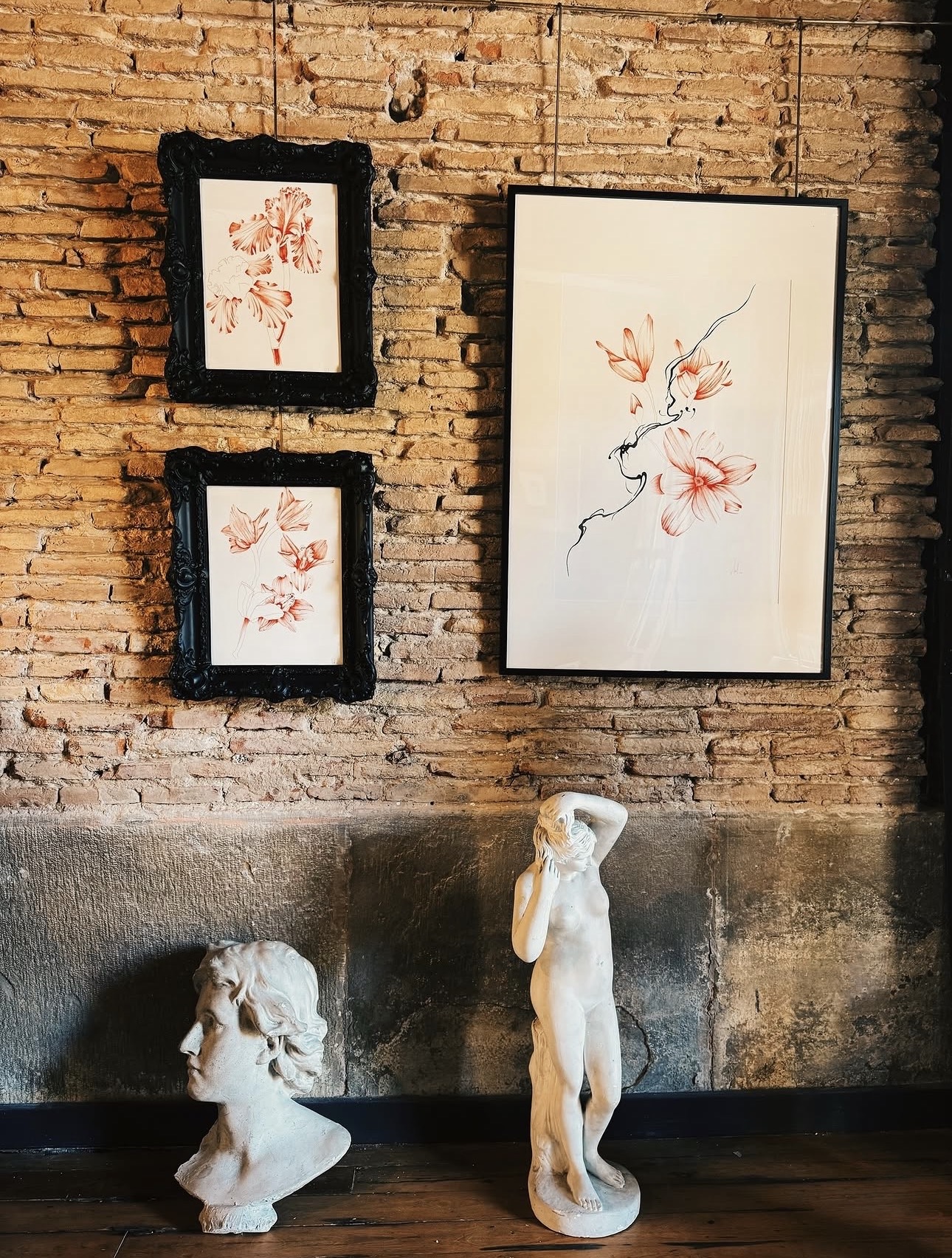 Dibujos de flores enmarcados sobre la pared de ladrillo, con dos esculturas debajo
